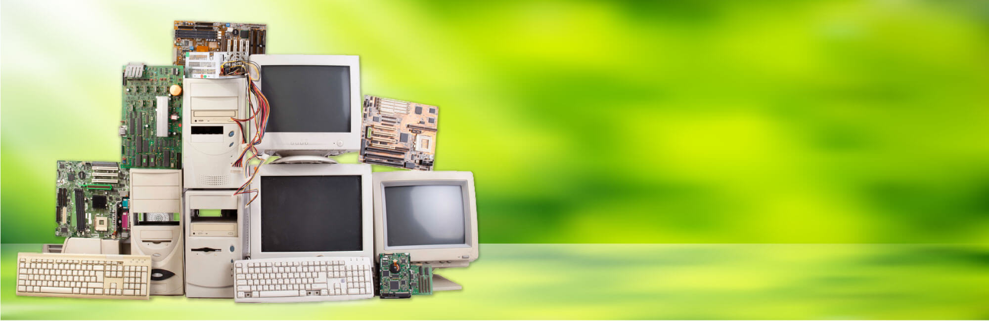 Pile of old computers, circut boards, and keyboards on a green background | Representing e-waste